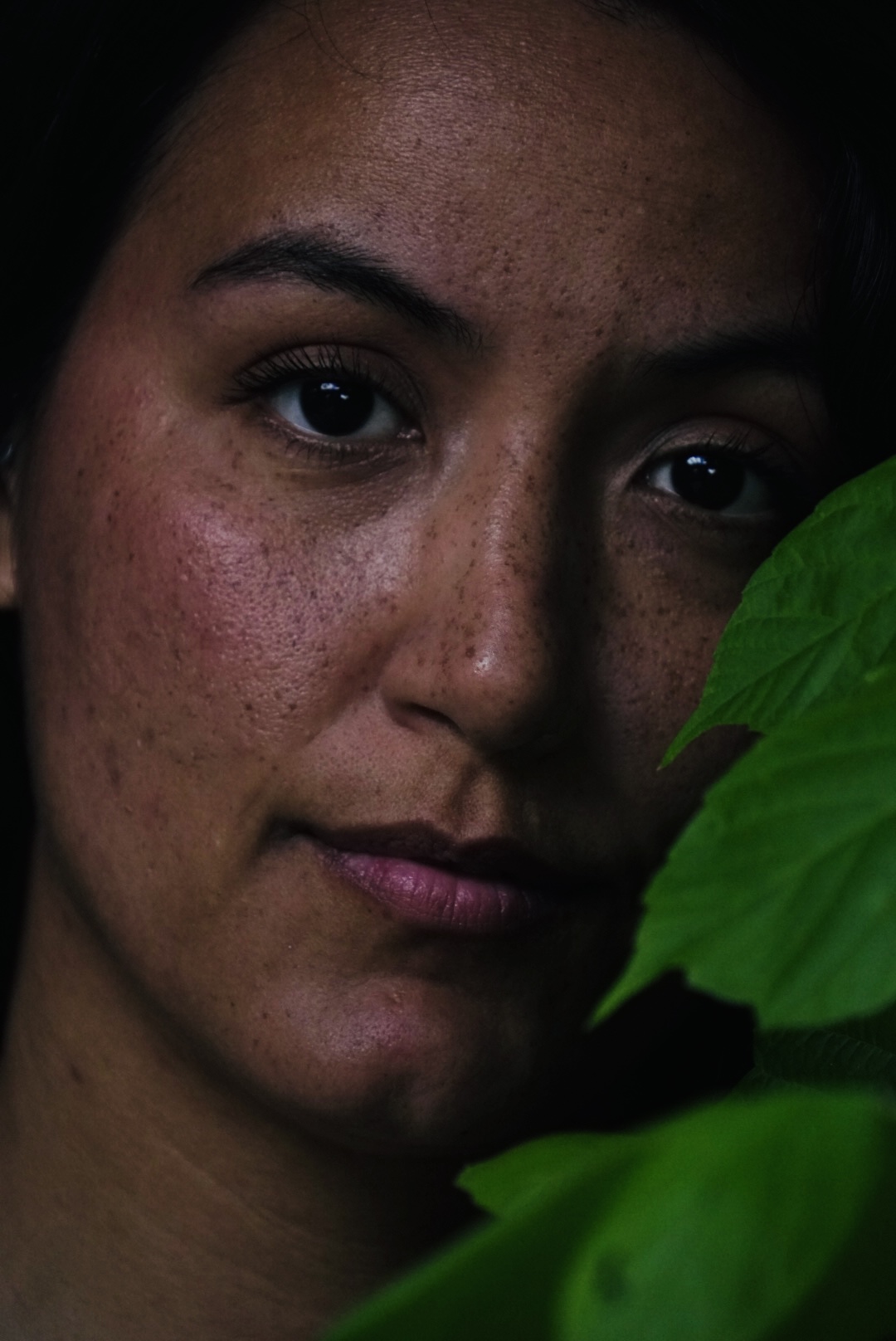 Low-light portrait partially framed by green leaves